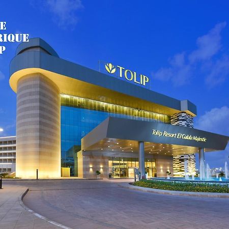 Tolip Resort El Galala Majestic Ajn-Szuhna Kültér fotó The photo shows a modern hotel building named "Tolip Resort & Spa," featuring a sleek architectural design with large glass windows. The hotel is illuminated against a twilight sky, showcasing its prominent signage. In the foreground, there is a well