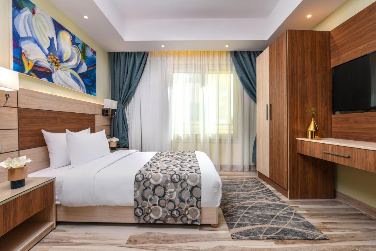 Tolip Resort El Galala Majestic Ajn-Szuhna Kültér fotó The photo shows a well-designed hotel room. It features a comfortable bed with a decorative bedspread and two pillows. There are soft curtains framing a window that lets in natural light. On one side, there is a colorful piece of artwork hanging on t