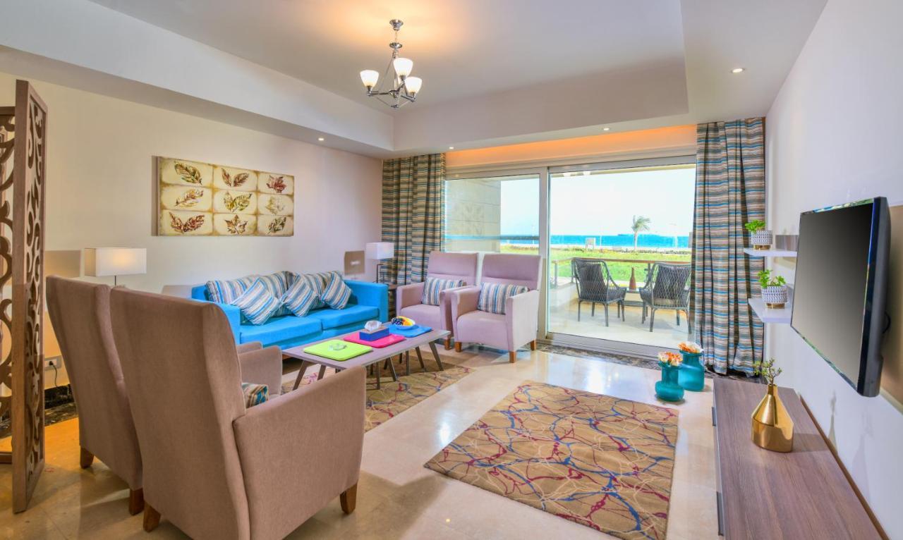 Tolip Resort El Galala Majestic Ajn-Szuhna Kültér fotó The photo shows a bright and modern living room. It features a blue sofa with decorative cushions, two light-colored armchairs, and a coffee table. A large area rug adds warmth to the space, which is decorated with a subtle pattern. The walls have so