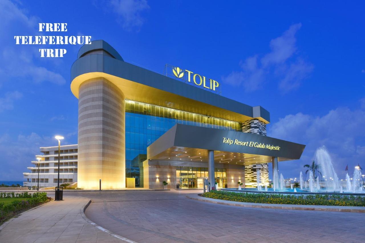 Tolip Resort El Galala Majestic Ajn-Szuhna Kültér fotó The photo shows a modern hotel building named "Tolip Resort & Spa," featuring a sleek architectural design with large glass windows. The hotel is illuminated against a twilight sky, showcasing its prominent signage. In the foreground, there is a well