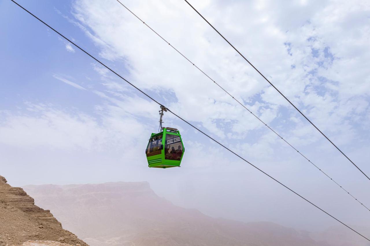 Tolip Resort El Galala Majestic Ajn-Szuhna Kültér fotó The photo shows a green cable car suspended in the air, traveling along overhead cables. The backdrop features a hazy landscape, likely mountainous or elevated terrain, with a cloudy sky. The scene suggests a scenic transportation method, possibly us