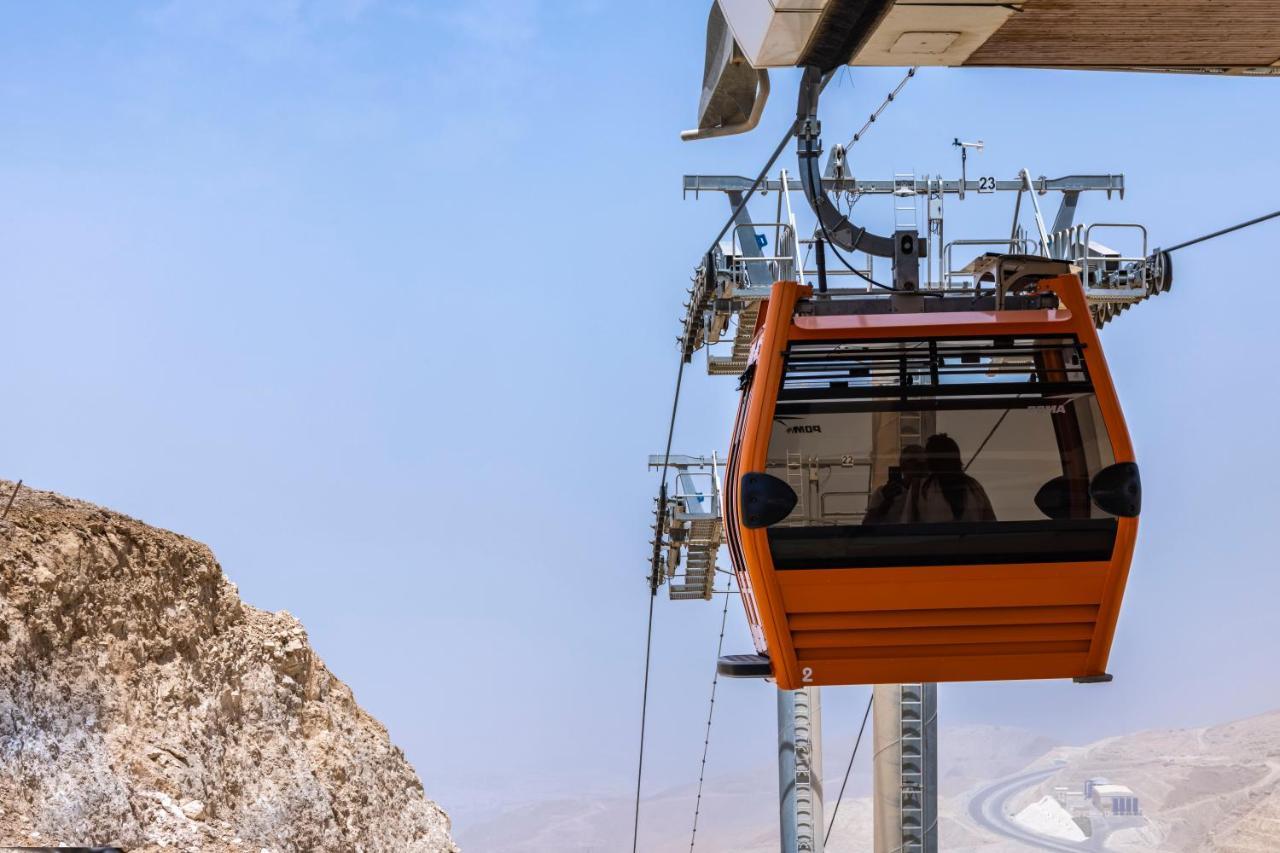 Tolip Resort El Galala Majestic Ajn-Szuhna Kültér fotó The photo shows an orange gondola or cable car hanging on a cable system. The gondola appears to be suspended in the air above a rocky landscape, with a clear sky in the background. There are supporting cables and structures visible, indicating that 