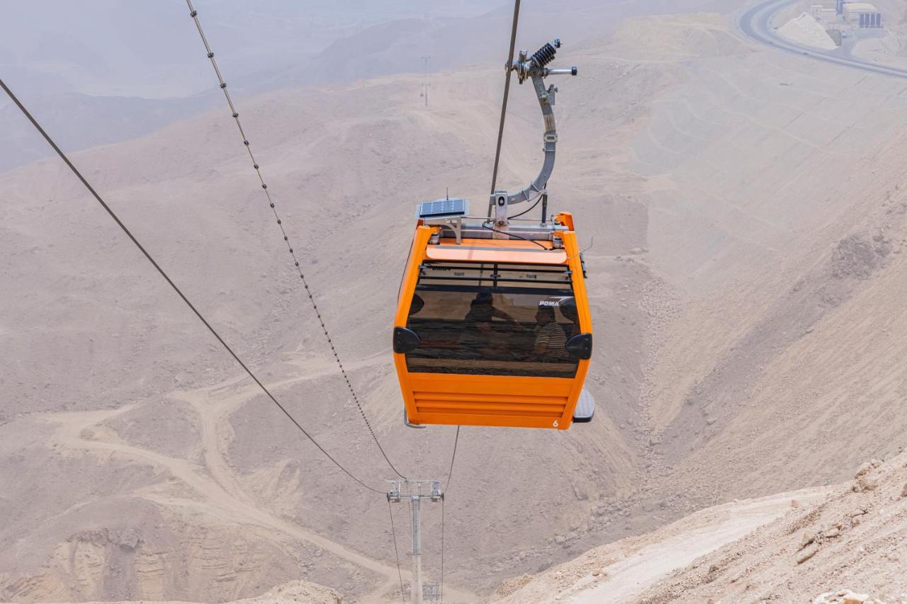 Tolip Resort El Galala Majestic Ajn-Szuhna Kültér fotó The photo shows an orange cable car suspended in the air, traveling along a set of cables. It appears to be located in a mountainous or hilly area, with rugged terrain and dry, rocky landscapes visible below. The background features slopes that seem 