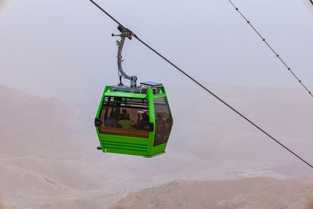 Tolip Resort El Galala Majestic Ajn-Szuhna Kültér fotó The photo shows a green cable car suspended in the air, moving along a wire. The cable car appears to be traversing a mountainous landscape, which looks rocky and arid. The surrounding environment is somewhat foggy or hazy, suggesting limited visibil