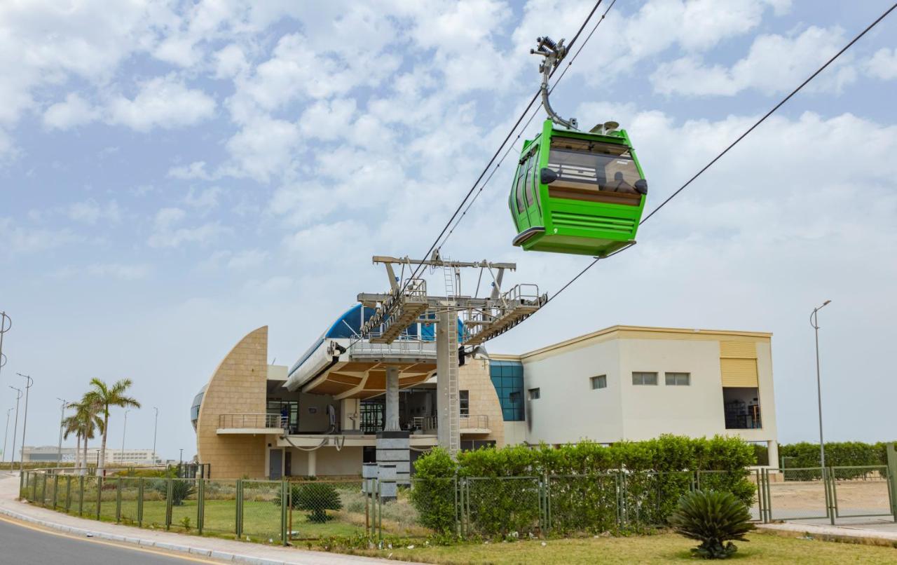 Tolip Resort El Galala Majestic Ajn-Szuhna Kültér fotó The photo shows a cable car or gondola system in operation, featuring a green-colored gondola. It is suspended from cables and moving towards a station, which appears to be a modern building with a unique architectural design. The station has large w