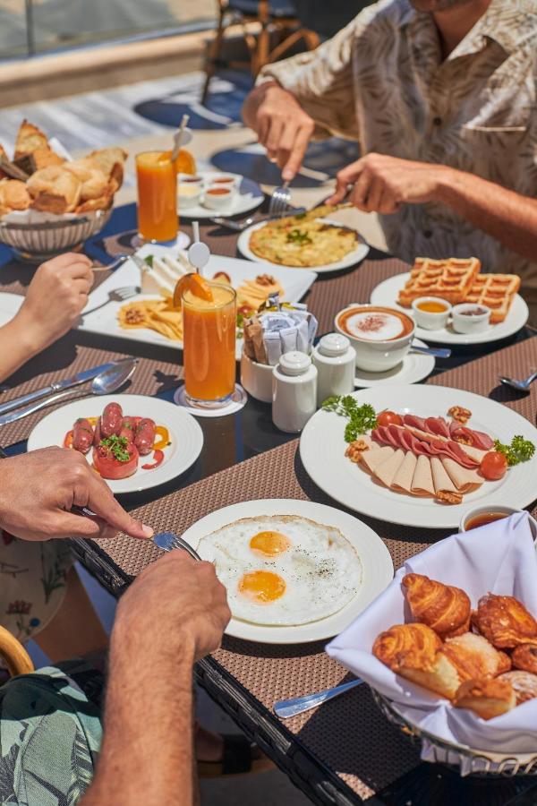 Tolip Resort El Galala Majestic Ajn-Szuhna Kültér fotó The photo features a spread of breakfast dishes on a table. There are two sunny-side-up eggs on one plate, surrounded by various food items, including slices of ham, sausages, and fresh tomatoes. Another plate holds a serving of waffles. A bowl with 