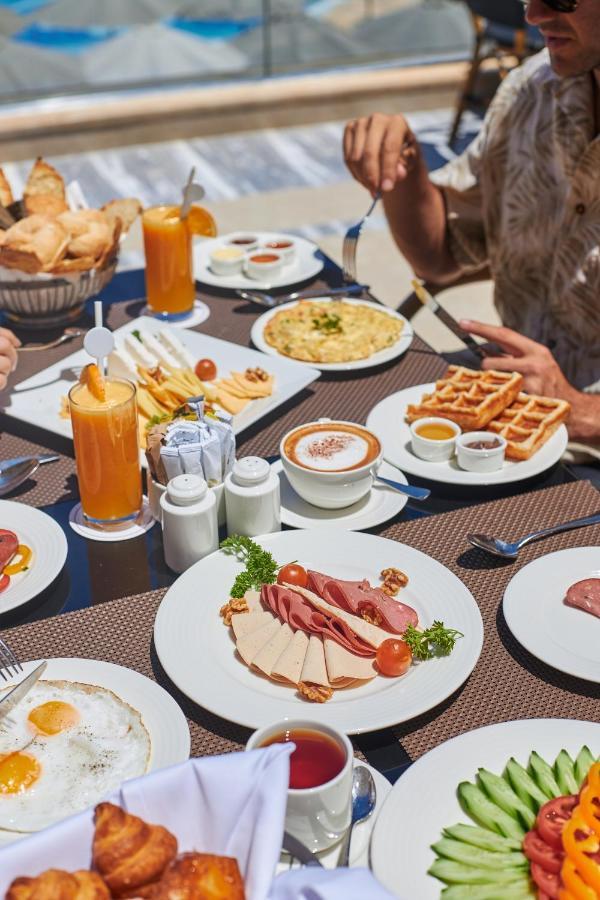 Tolip Resort El Galala Majestic Ajn-Szuhna Kültér fotó The photo shows a breakfast spread laid out on a table. There are several plates with a variety of food items, including:

1. **Sliced Cold Cuts**: A plate featuring various cold meats, accompanied by garnishes like cherry tomatoes and lettuce.
2. **