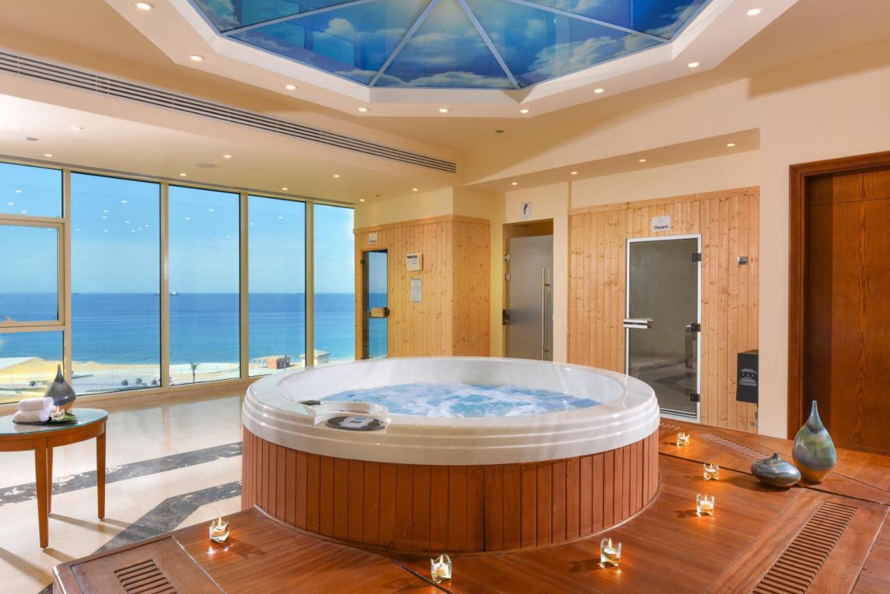 Tolip Resort El Galala Majestic Ajn-Szuhna Kültér fotó The photo shows a luxurious spa room featuring a large, round hot tub positioned in the center. The walls are mostly glass, offering a stunning view of the ocean. The ceiling has a painted sky, enhancing the serene atmosphere. There are wooden elemen