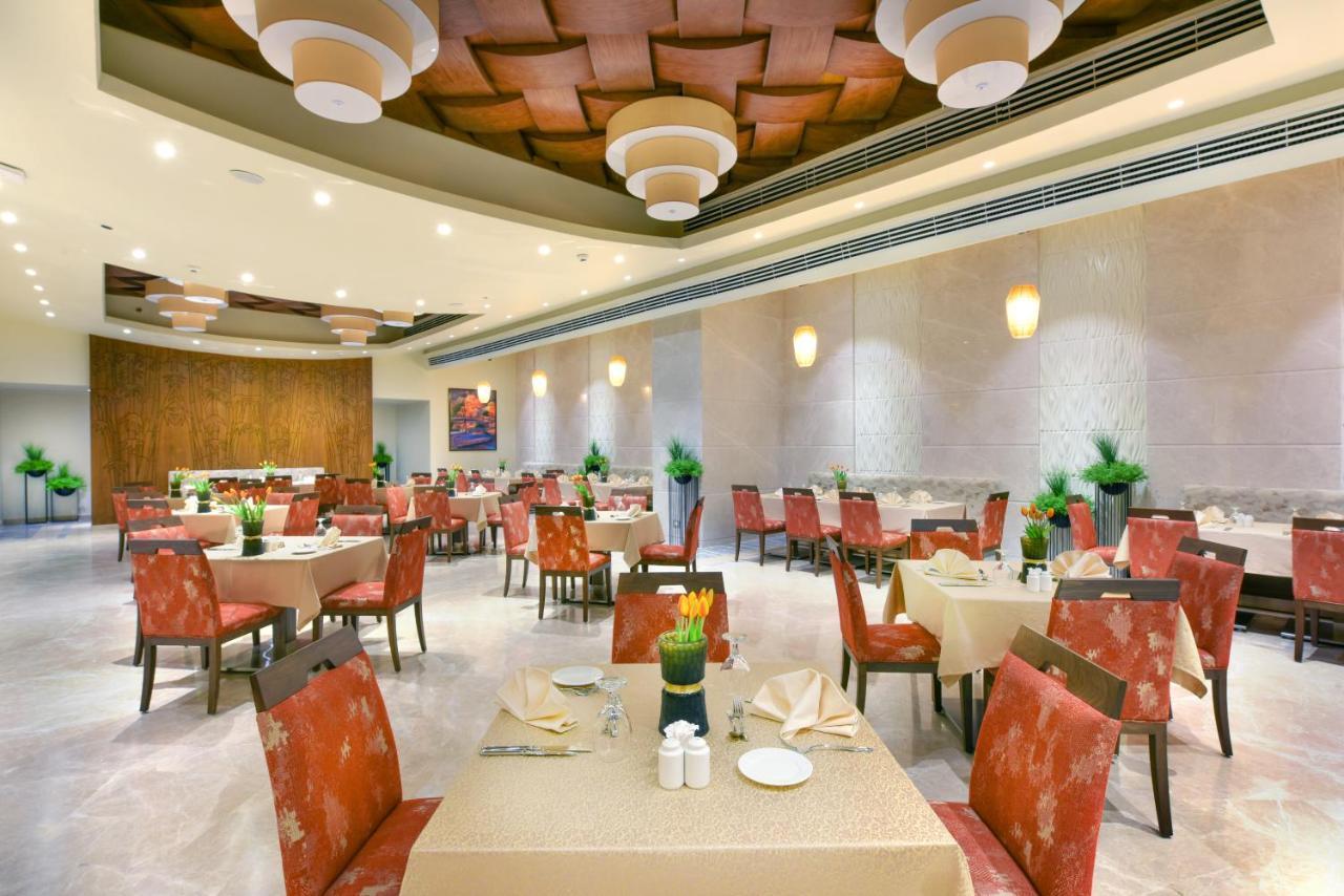 Tolip Resort El Galala Majestic Ajn-Szuhna Kültér fotó The photo shows the interior of a restaurant. The space features several tables set with light-colored tablecloths and chairs with reddish upholstery. Each table is adorned with decorative napkins and has small plants in the center. The room has a mo