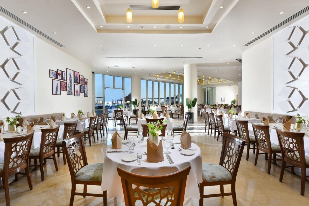 Tolip Resort El Galala Majestic Ajn-Szuhna Kültér fotó The photo displays a spacious and elegantly designed restaurant interior. It features numerous tables set for dining, with white tablecloths, neatly folded napkins, and decorative centerpieces of flowers. The seating consists of wooden chairs that co