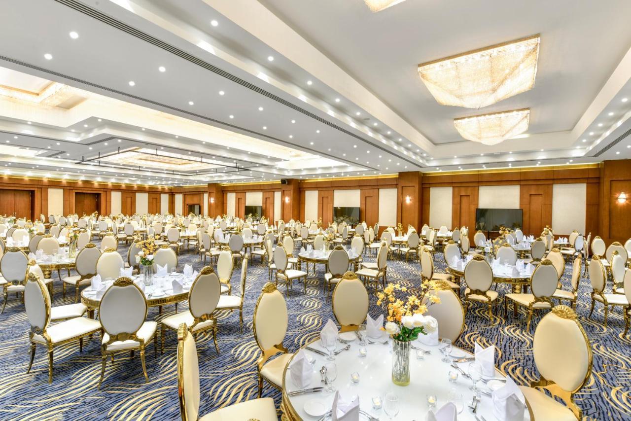 Tolip Resort El Galala Majestic Ajn-Szuhna Kültér fotó The photo shows a spacious and elegantly decorated banquet hall. The room features numerous round dining tables, each set with white tablecloths and adorned with decorative centerpieces, likely flowers. The chairs surrounding the tables have a luxuri
